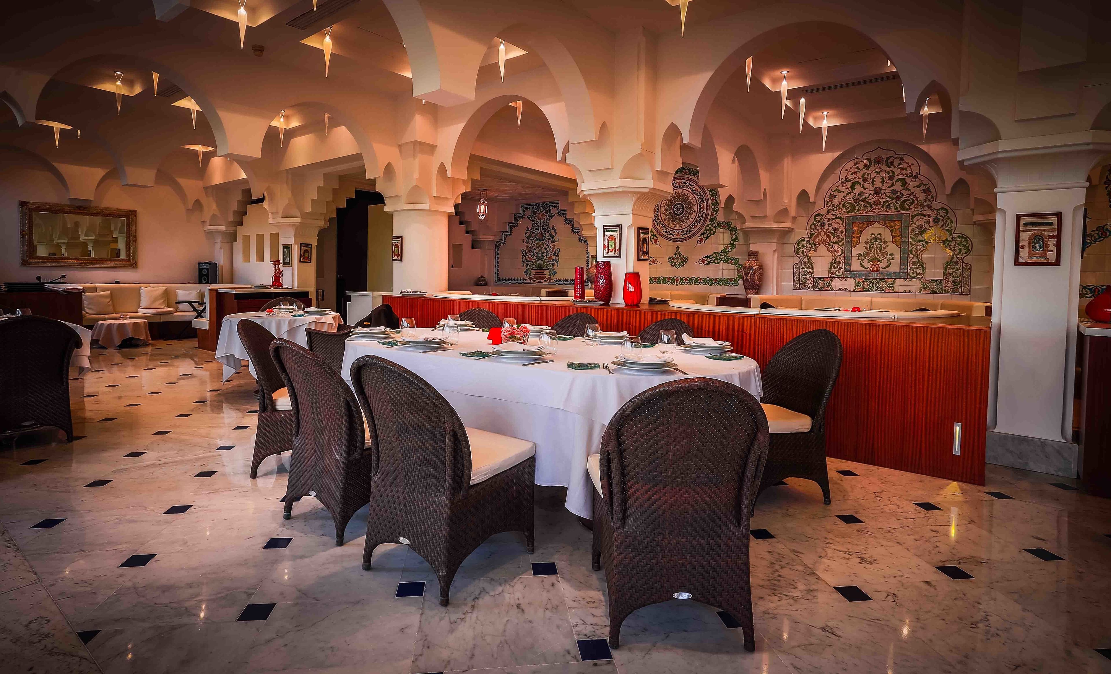 Un restaurant avec des tables rondes, des chaises en osier et un comptoir rouge.