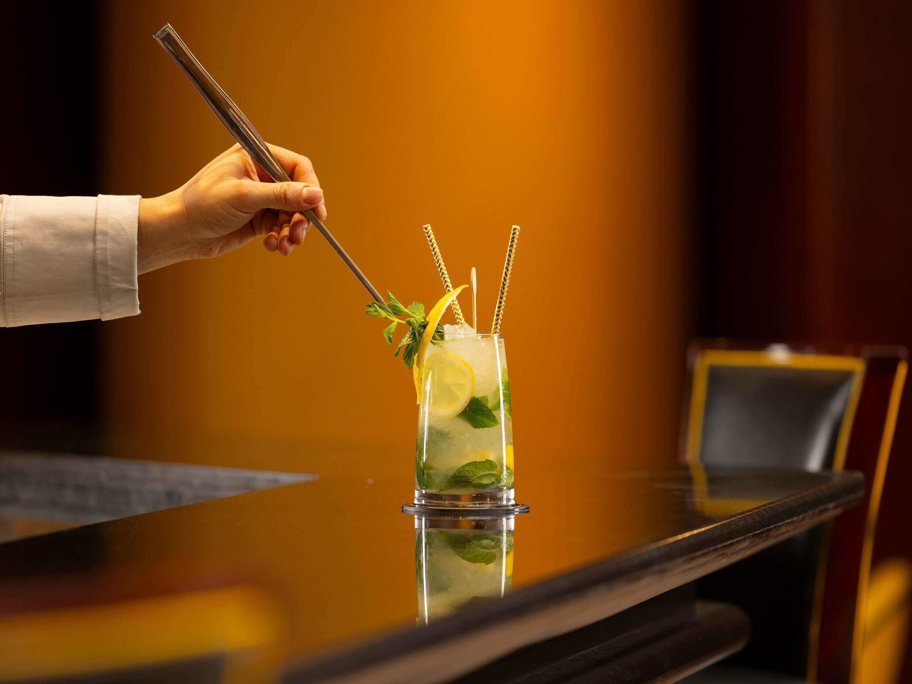 A hand holding a cocktail shaker, preparing a drink with lemon slices and mint leaves.