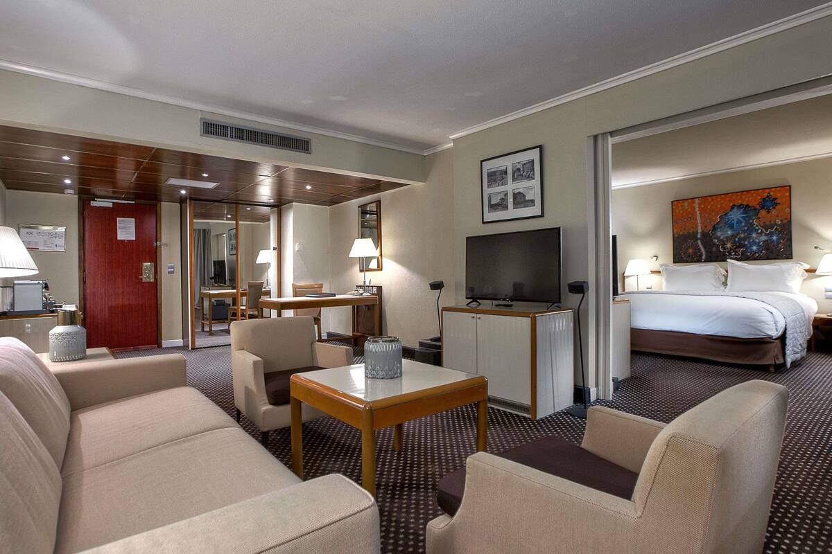 A hotel room with a bed, a desk with a TV, a dining area with chairs, and a sofa.