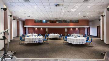 Une salle de conférence dotée de plusieurs tables et chaises, d’un sol recouvert de moquette et d’un plafond haut avec des luminaires encastrés.