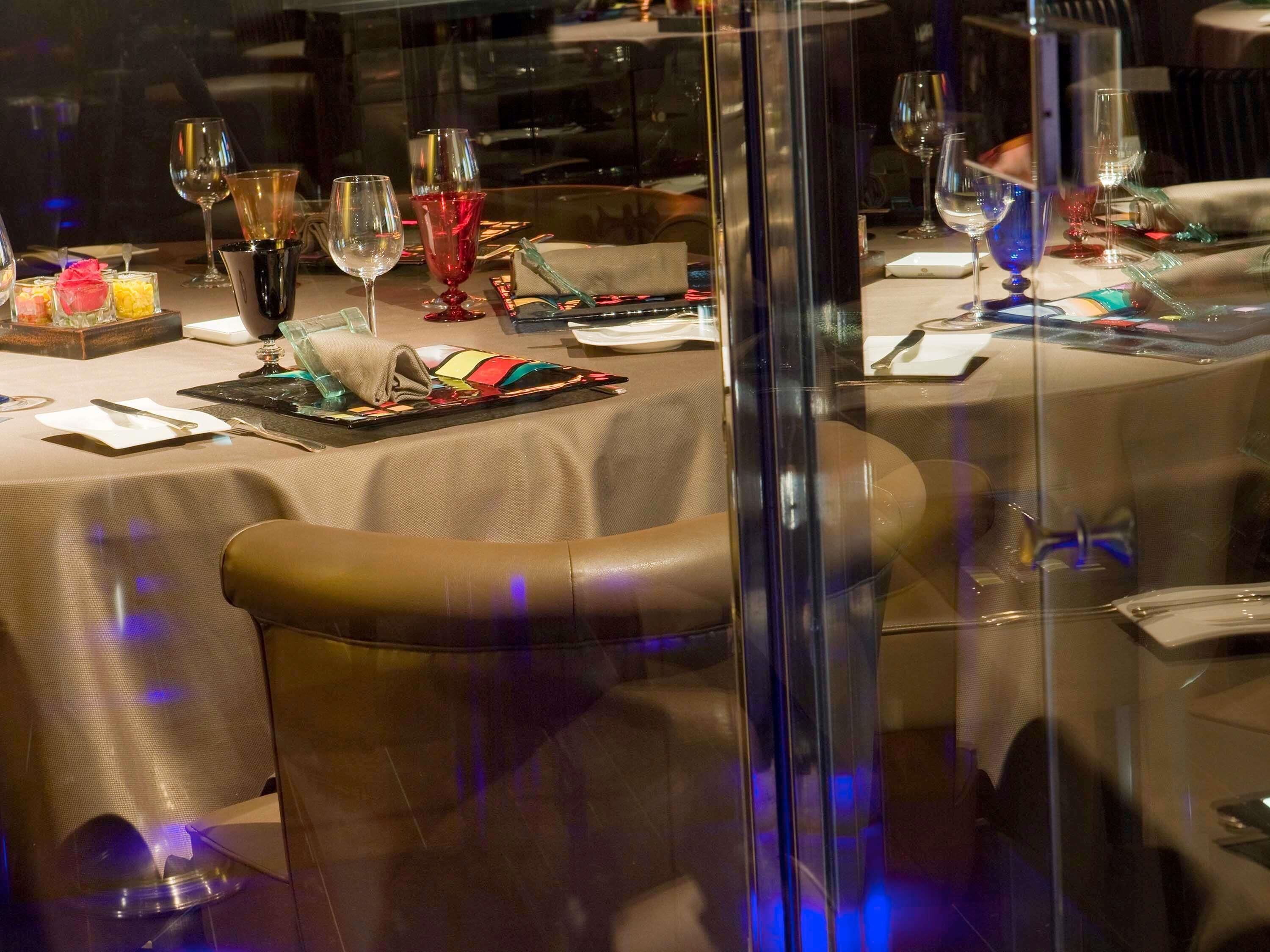 A restaurant with tables set for dining, featuring glass partitions and leather chairs.