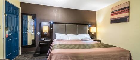 Quarto de hotel com cama, escrivaninha, espelho e porta.