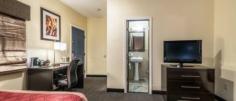 Quarto de hotel com duas camas, uma escrivaninha, uma cadeira, televisão e banheiro.