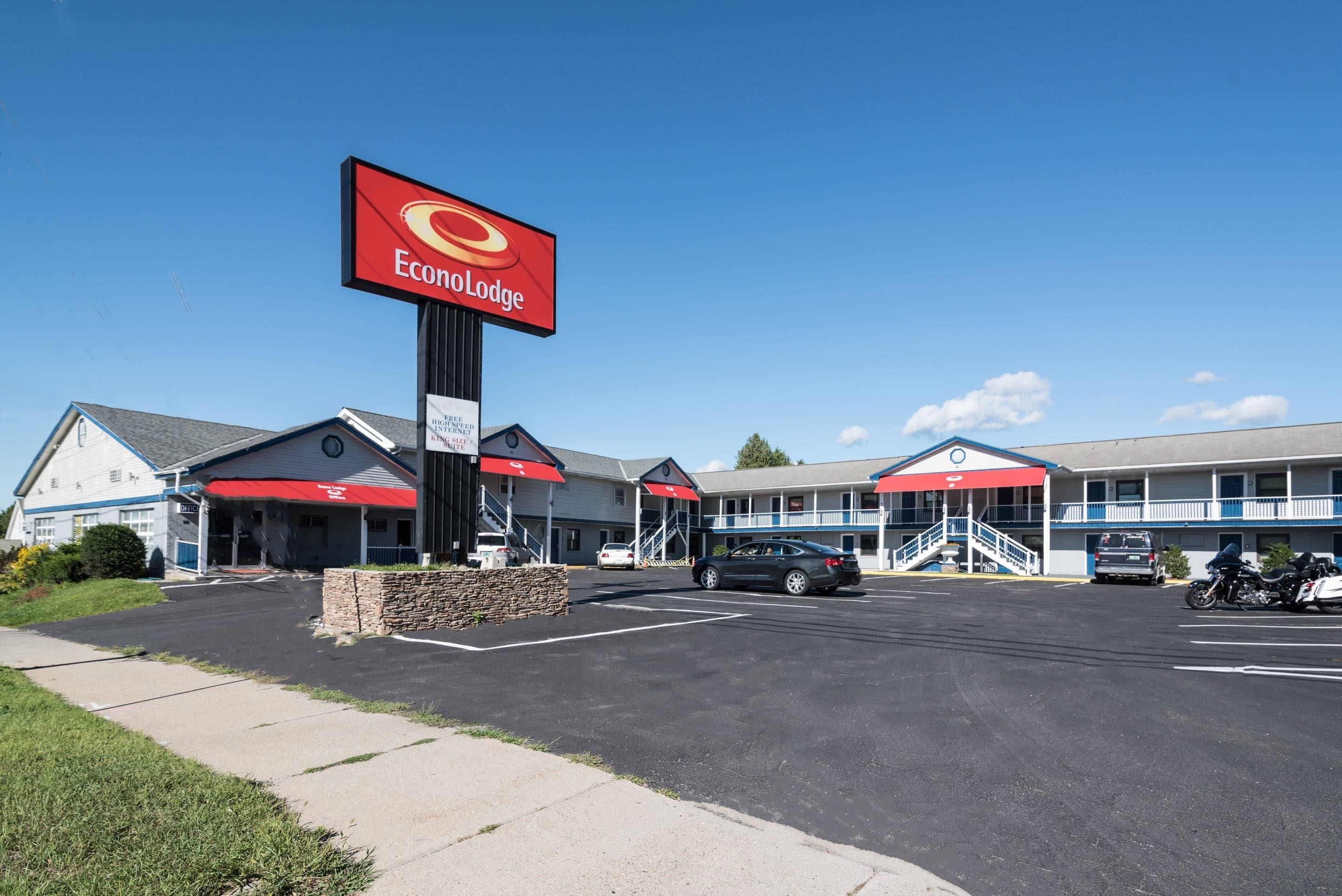 A motel with a prominent red sign, multiple parking spaces, and a clear sky.