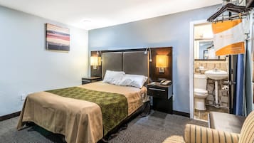 A hotel room with a bed, bedside tables, a lamp, a chair, and a bathroom visible through an open door.