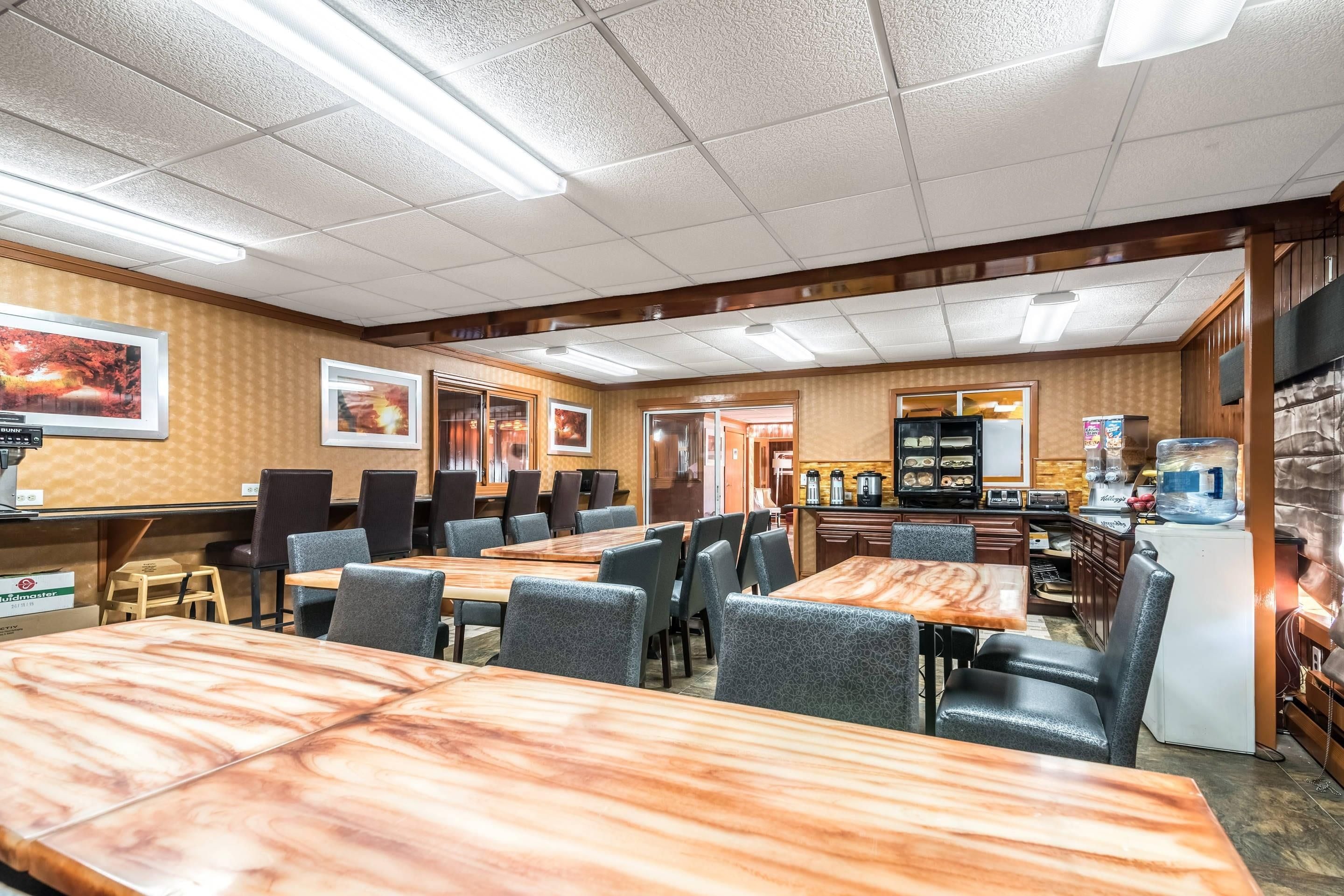 Un restaurant doté de nombreuses tables et chaises, d’un espace cuisine et de tableaux encadrés aux murs.