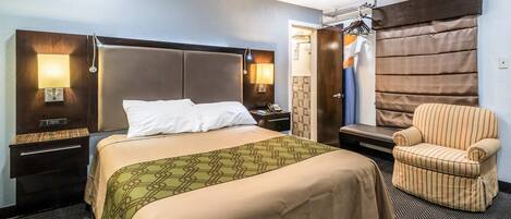 Habitación de hotel con cama, mesitas de noche, una silla, armario y baño visible a través de una puerta abierta.