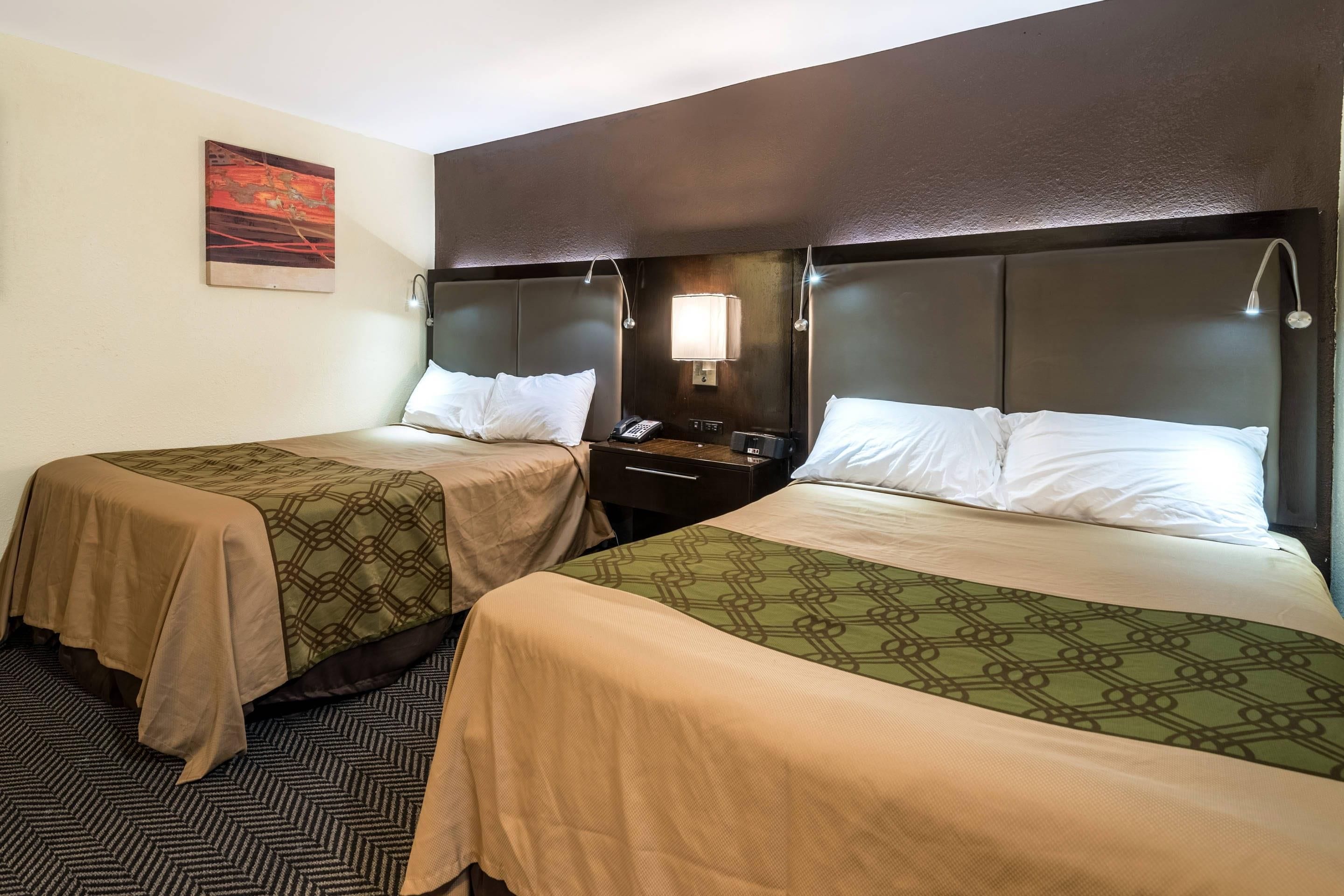 A hotel room with two beds, each with a headboard, bedside tables, lamps, and a painting on the wall.