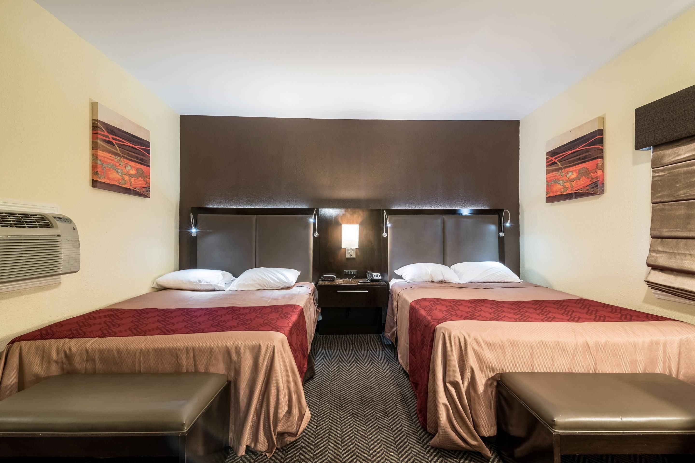 A hotel room with two beds, a nightstand, a desk, and a bench.