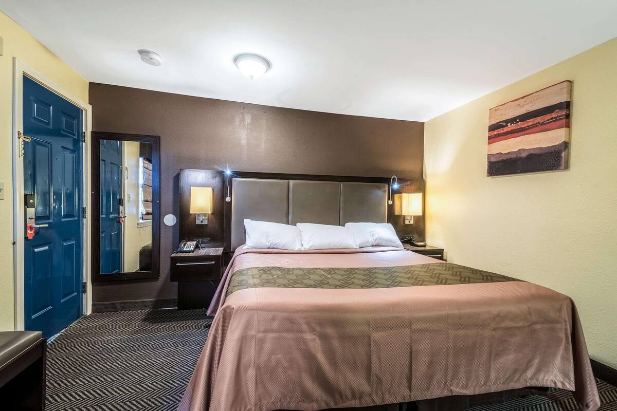 A hotel room with a bed, a nightstand, a phone, a mirror, and a painting on the wall.