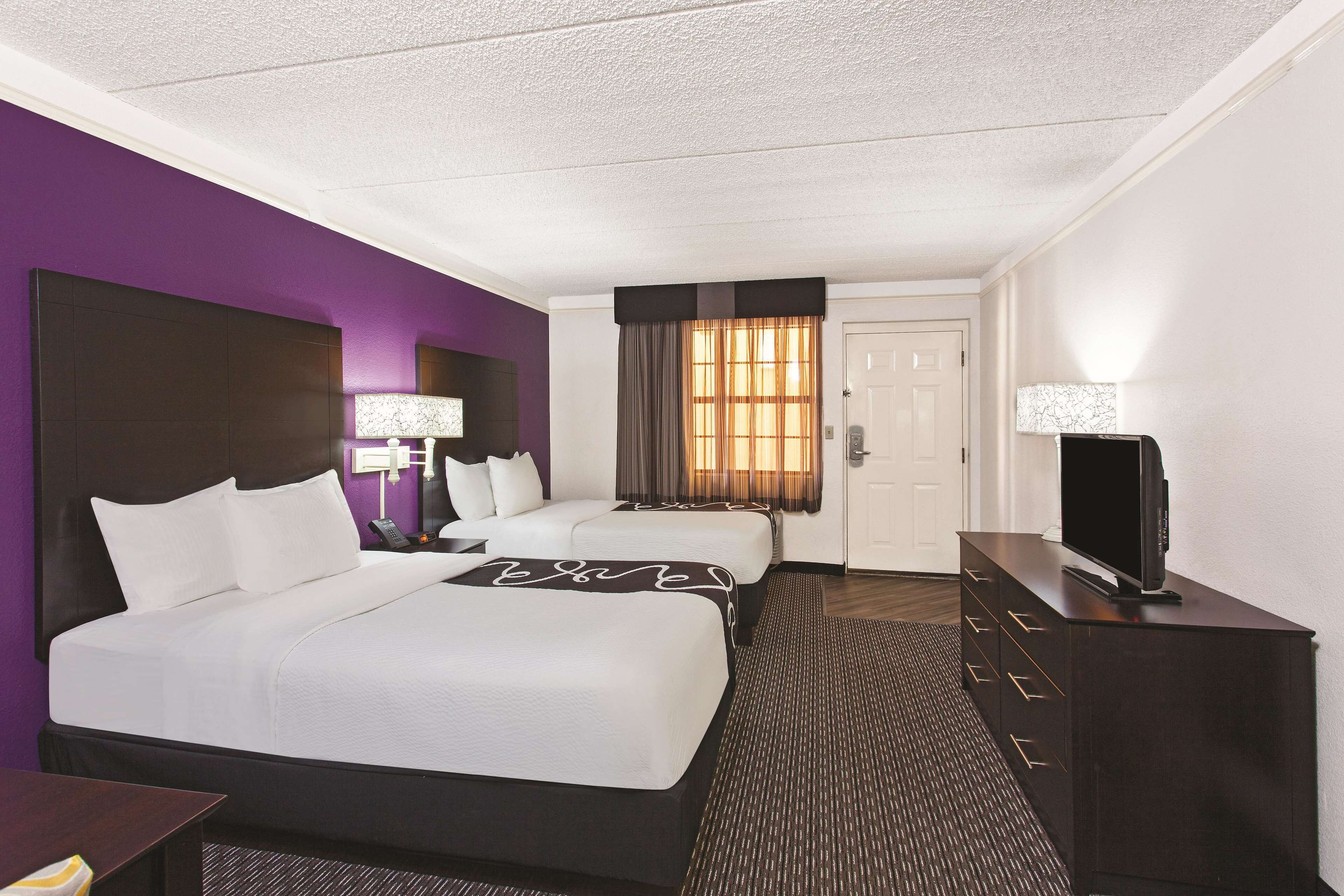 A hotel room with two beds, a TV, a dresser, and a window with curtains.