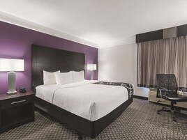 A hotel room with a large bed, two bedside tables with lamps, a chair, and a window with curtains.