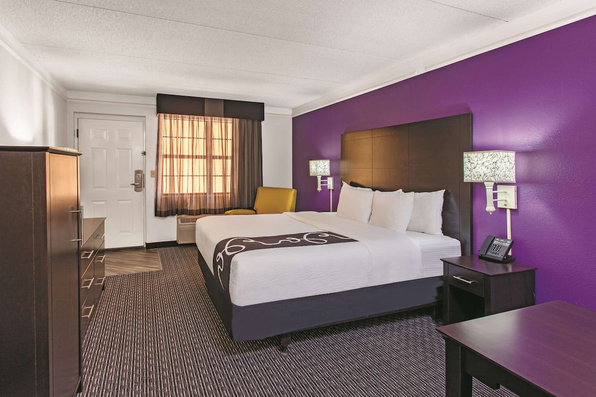 A hotel room with a bed, a chair, a desk, and a nightstand with a phone.