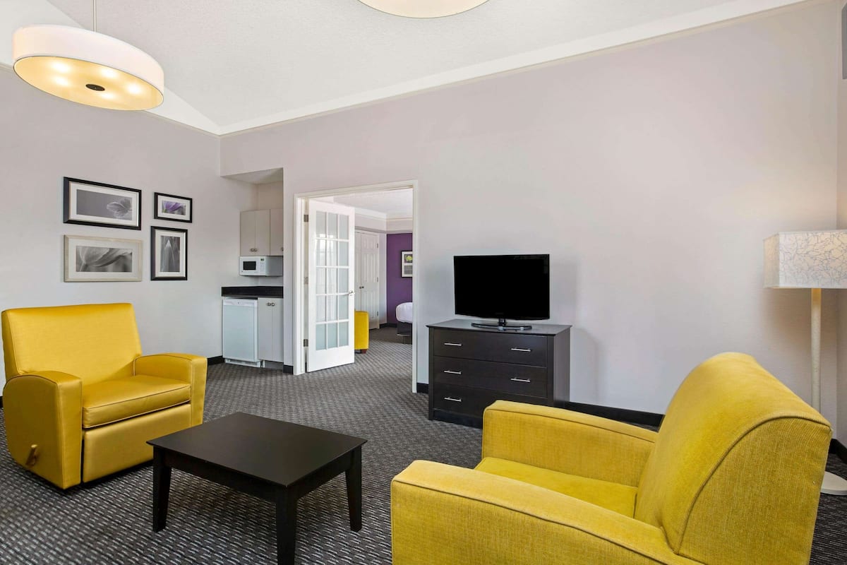 A hotel room with a yellow sofa, a black coffee table, a flat-screen TV, a small cabinet, and a microwave in the background.