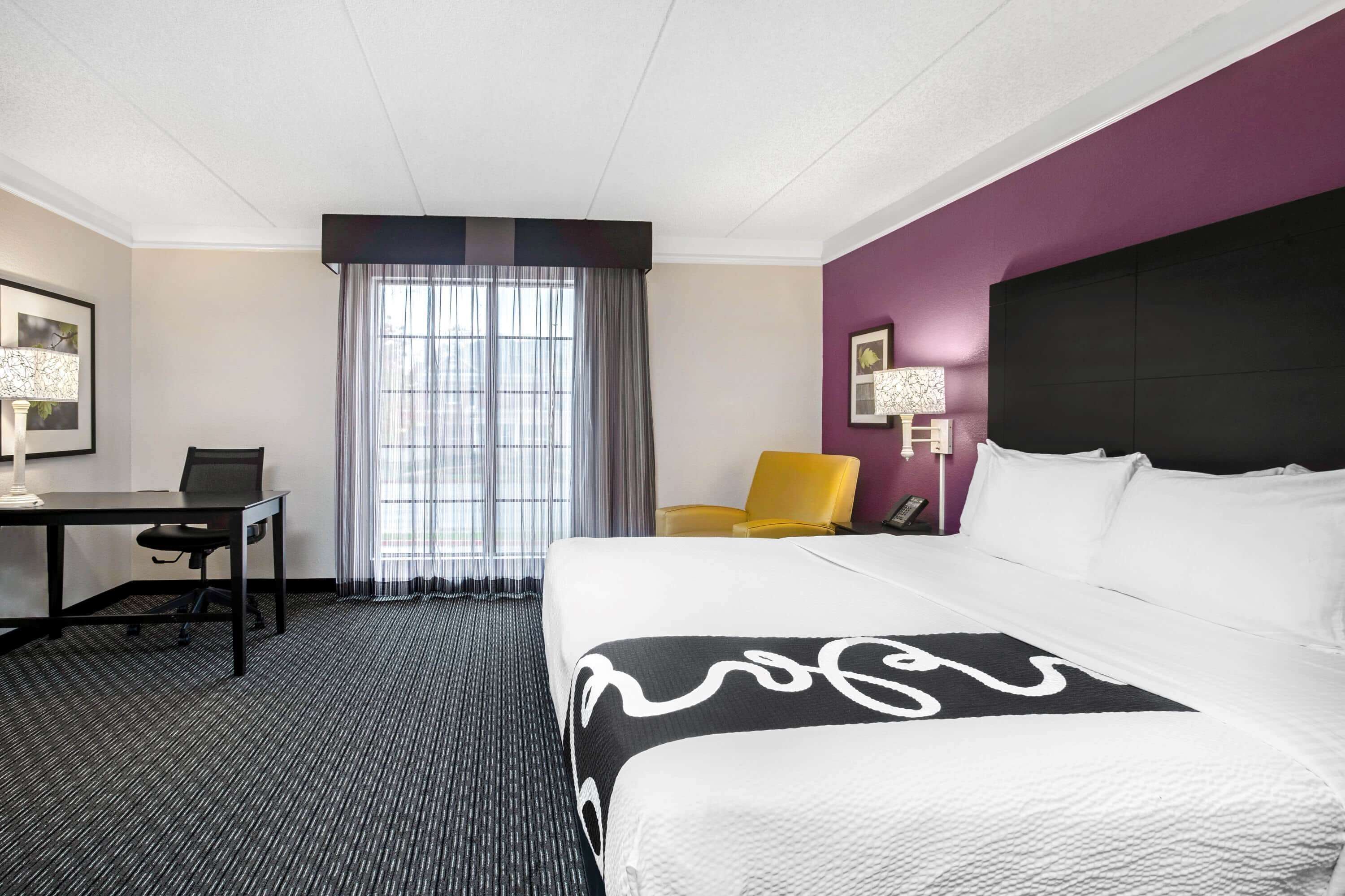 A hotel room with a large bed, a desk, a chair, and a window with curtains.