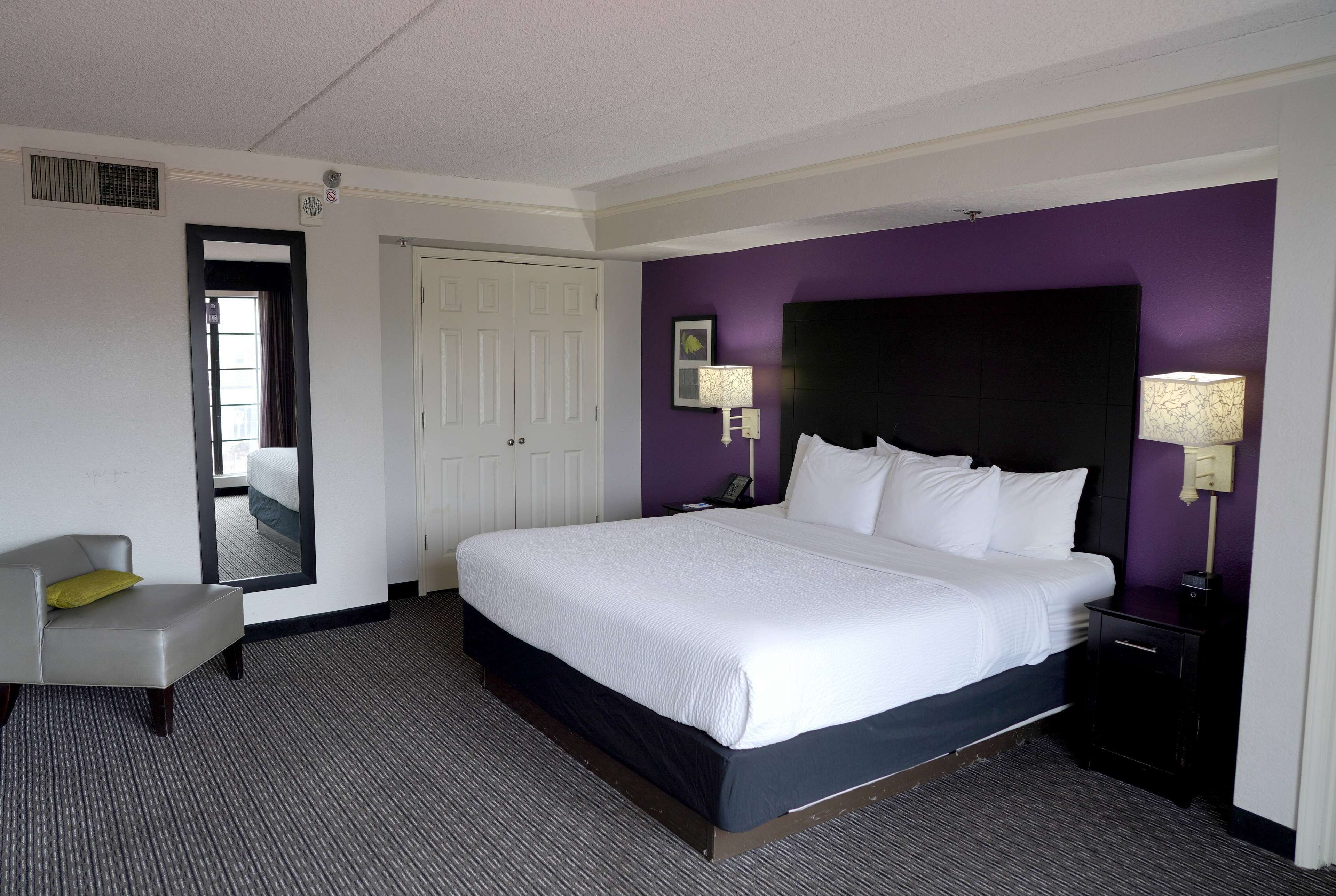 A hotel room with a large bed, a chair, a nightstand, and a mirror.