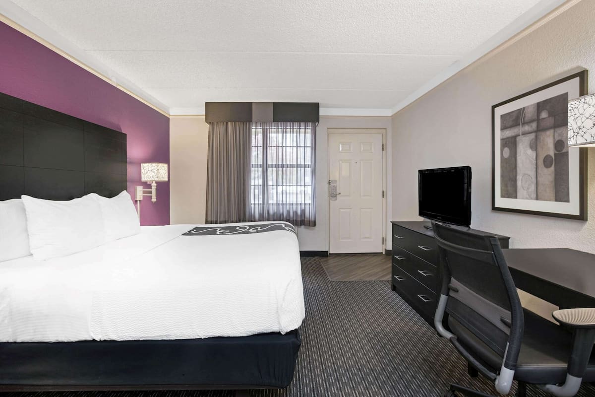 A hotel room with a bed, a desk, a chair, a television, and a door.