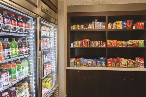 A beverage cooler stocked with various sodas and a shelf with snacks and cereals.