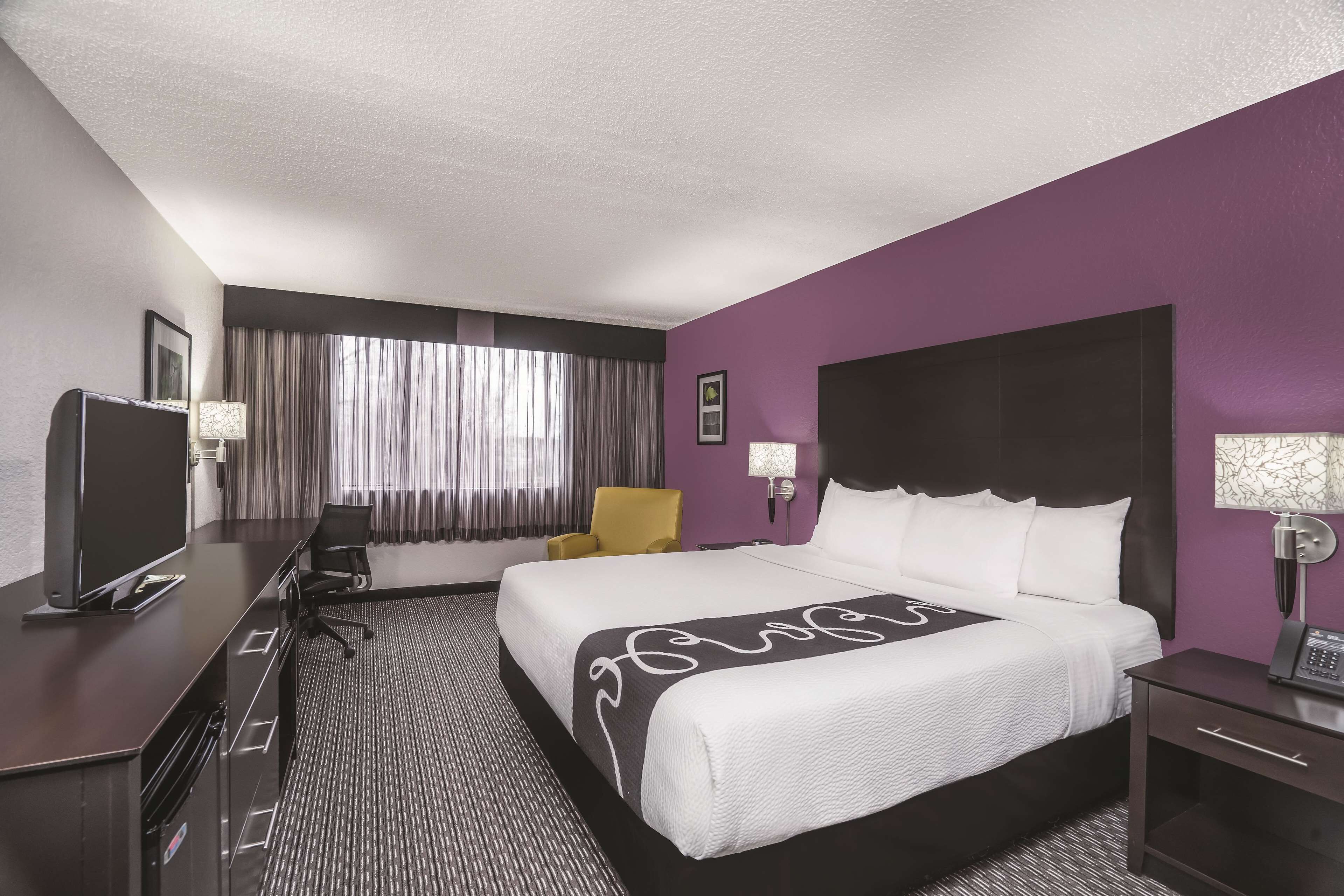 Una habitación de hotel con una cama grande, un escritorio con computadora, una silla y un televisor.