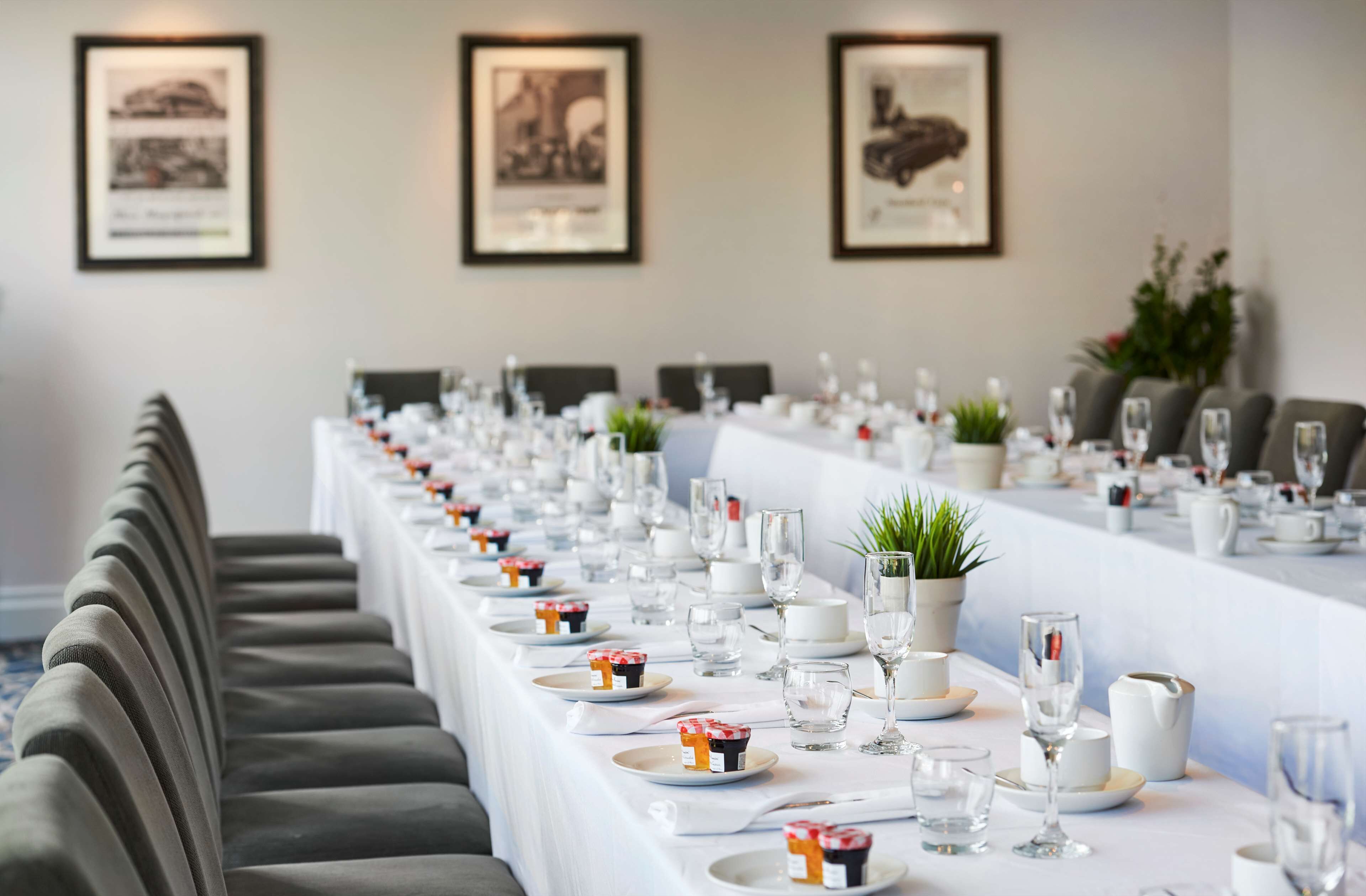 A long dining table set with plates, glasses, and small decorative items, flanked by cushioned chairs.