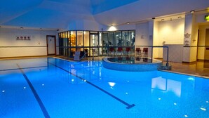 Piscina interior com pistas demarcadas, área de vestiários e espaço de descanso com cadeiras.