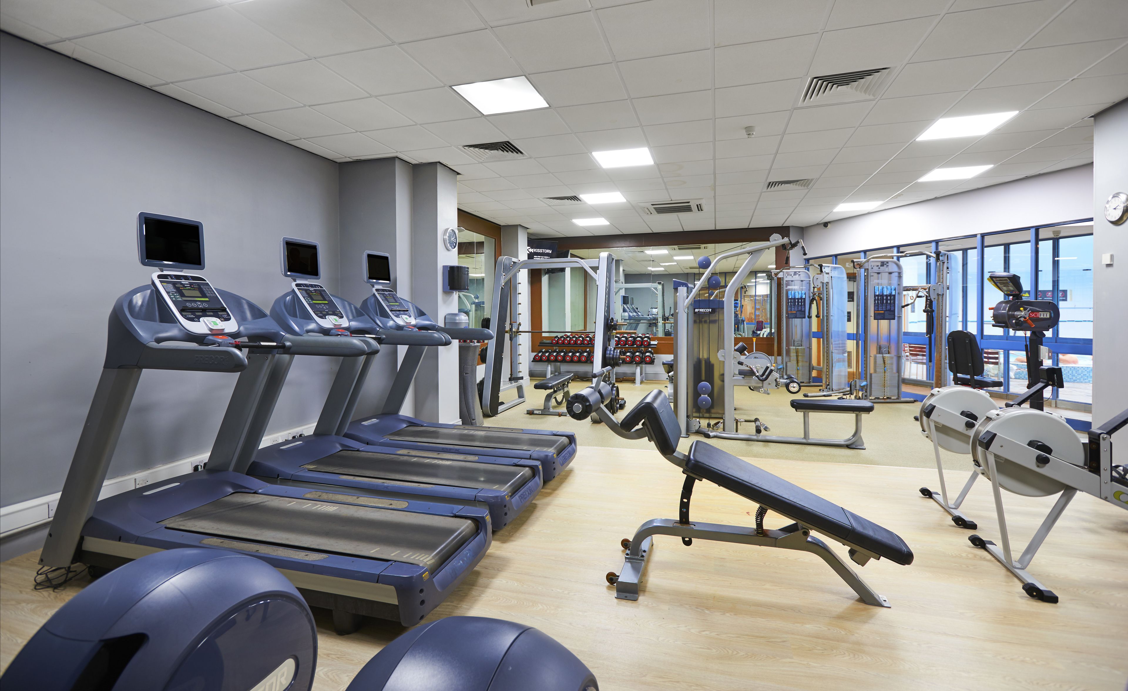 Un gimnasio con cintas de correr, máquinas de pesas y un muro de espejos.