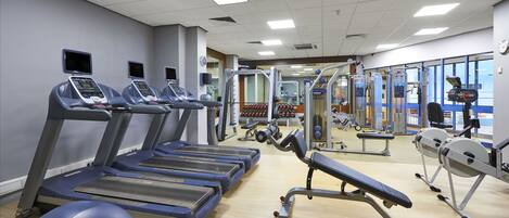 Un gimnasio con cintas de correr, máquinas de pesas y un muro de espejos.