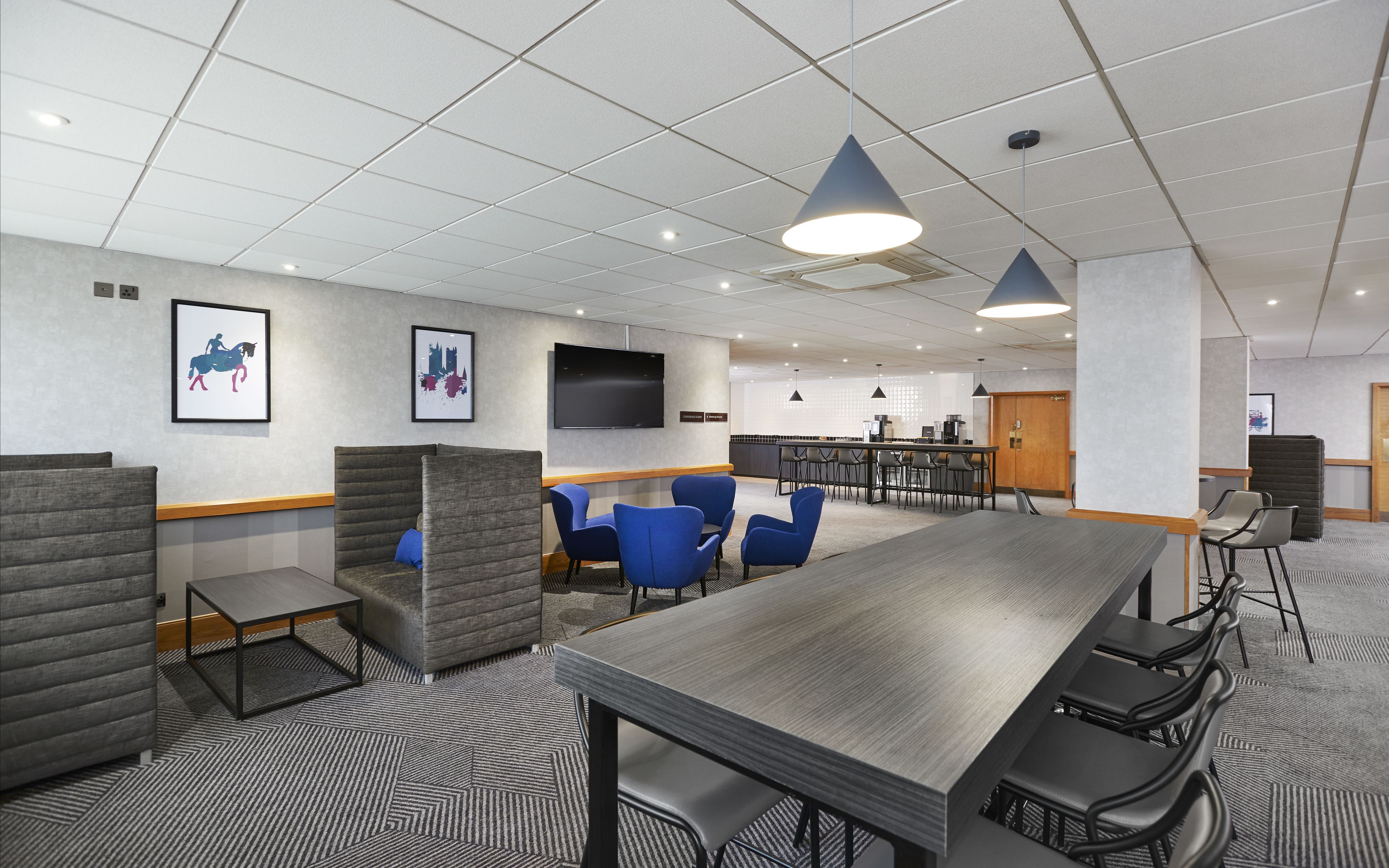 A modern conference room with a long table, blue chairs, and gray cushioned seating.