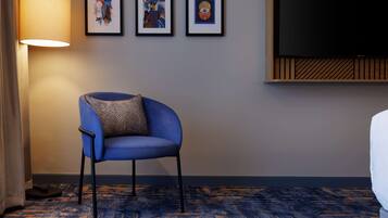 Una habitación de hotel con un sillón azul, una lámpara de pie grande y tres cuadros en la pared.