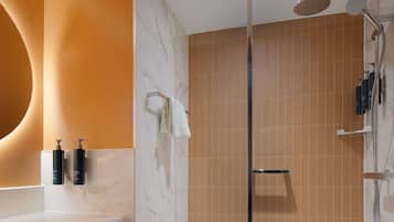 Un baño moderno con ducha envuelta en vidrio, tocador de mármol y un espejo grande.