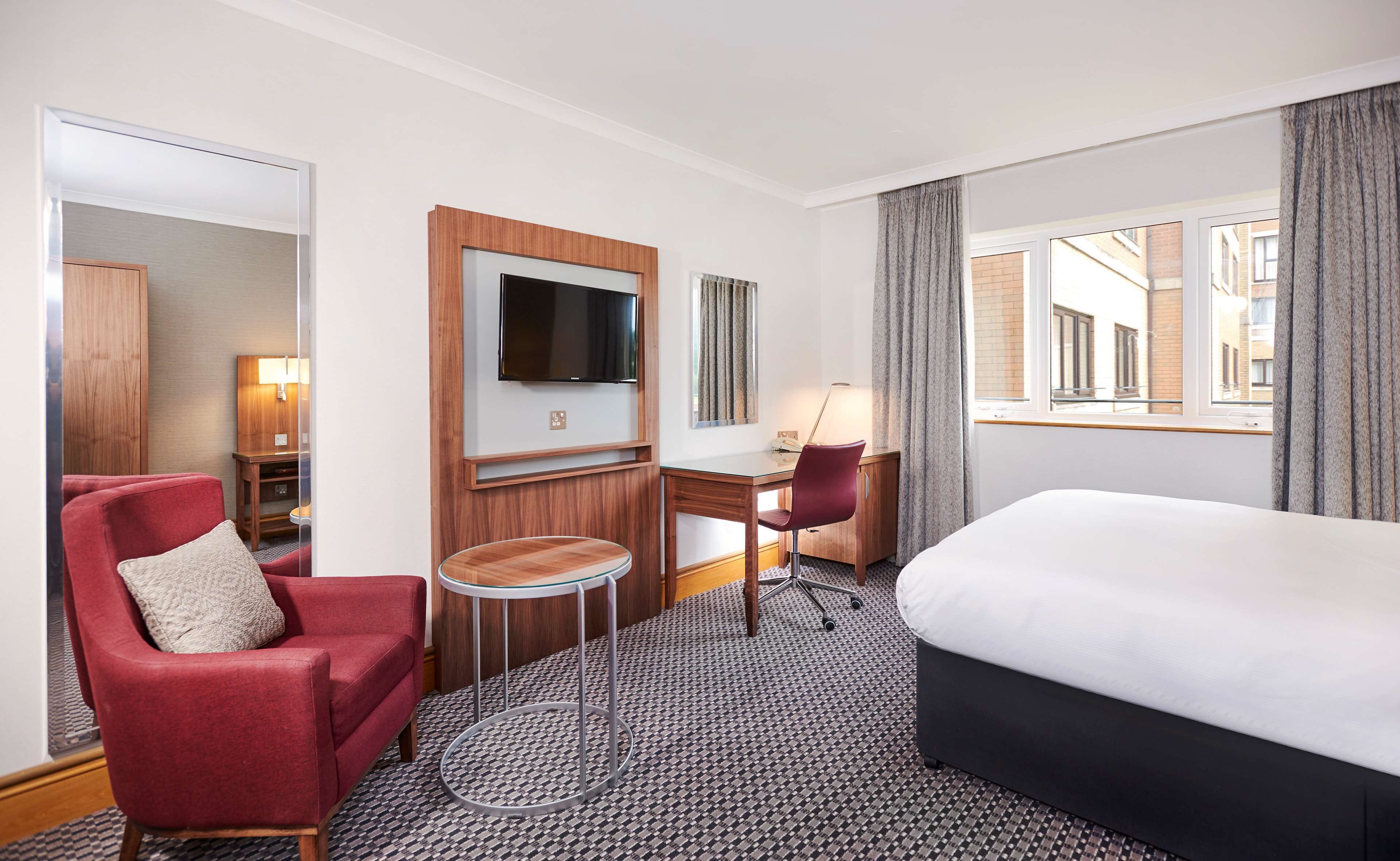 Een hotelkamer met een bed, een bureau, een stoel, een televisie en uitzicht op de stad.