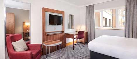 A hotel room with a bed, a desk, a chair, a TV, and a view of the city.