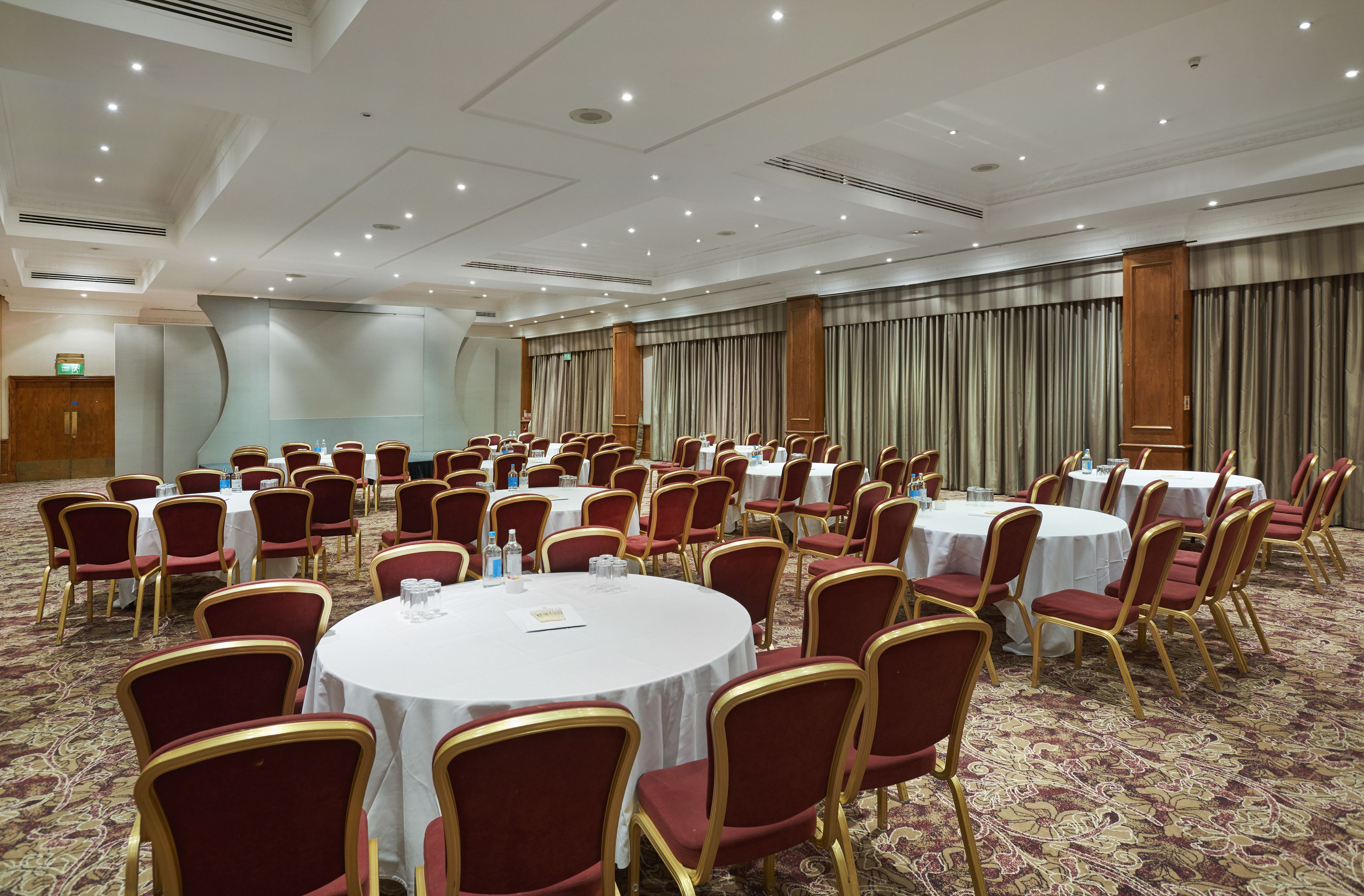 Ein Konferenzraum mit runden Tischen und roten Stühlen, mit Teppichboden und einer großen Stoffkulisse.