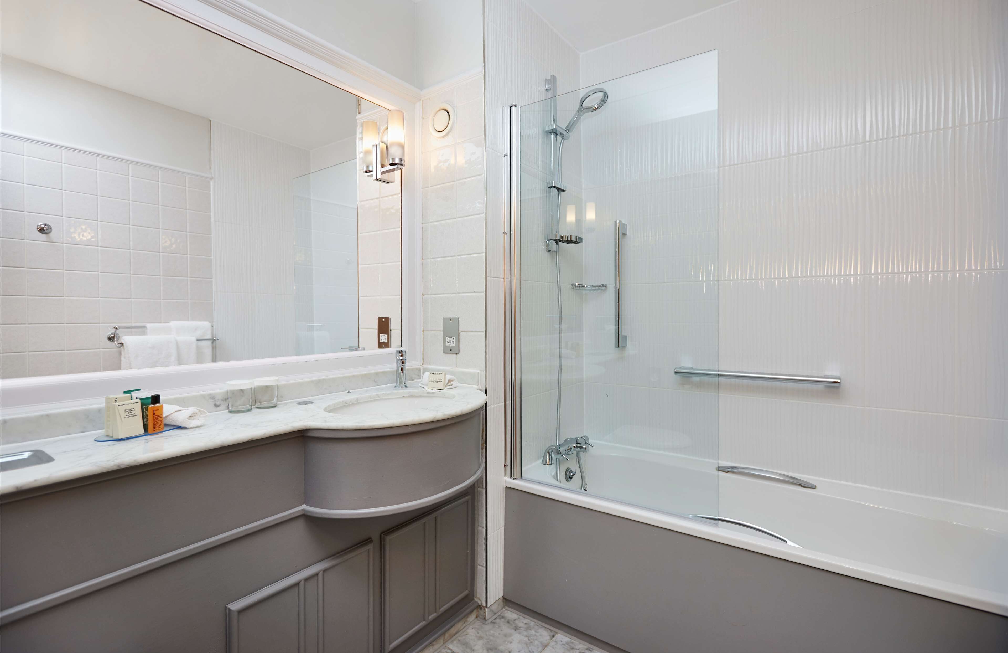 A modern bathroom with a glass-enclosed shower, a large mirror, and a curved vanity with a sink.