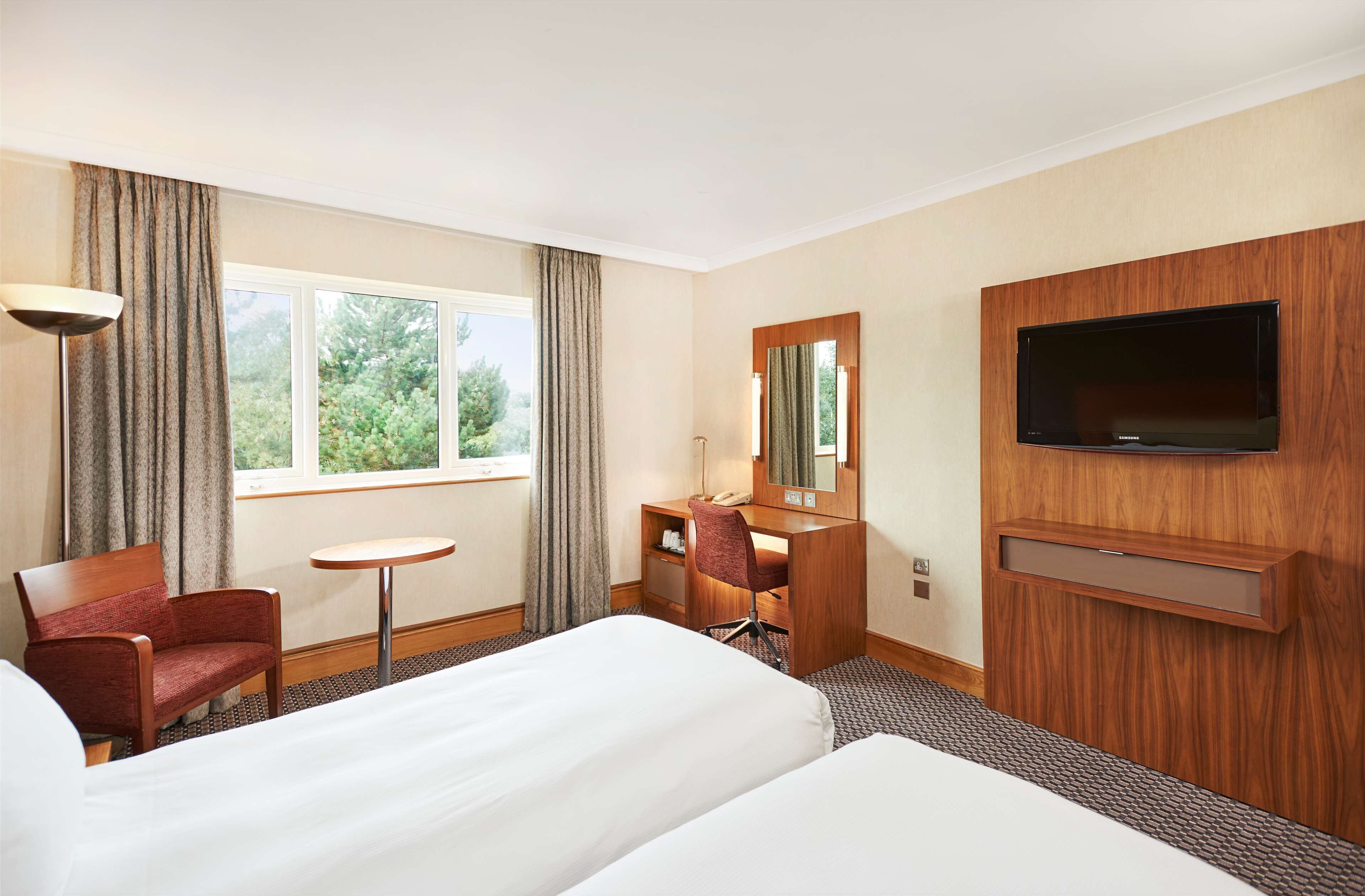A hotel room with two beds, a desk, a chair, a television, and a window with curtains.
