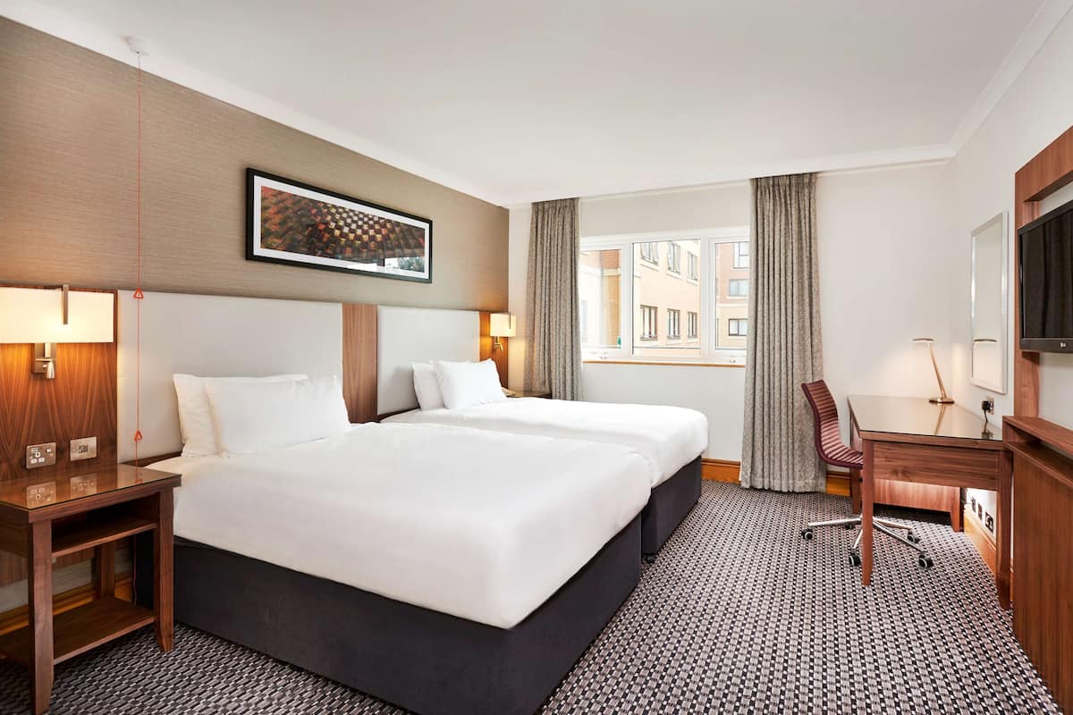 A hotel room with a large bed, a desk, a chair, a TV, and a window with curtains.