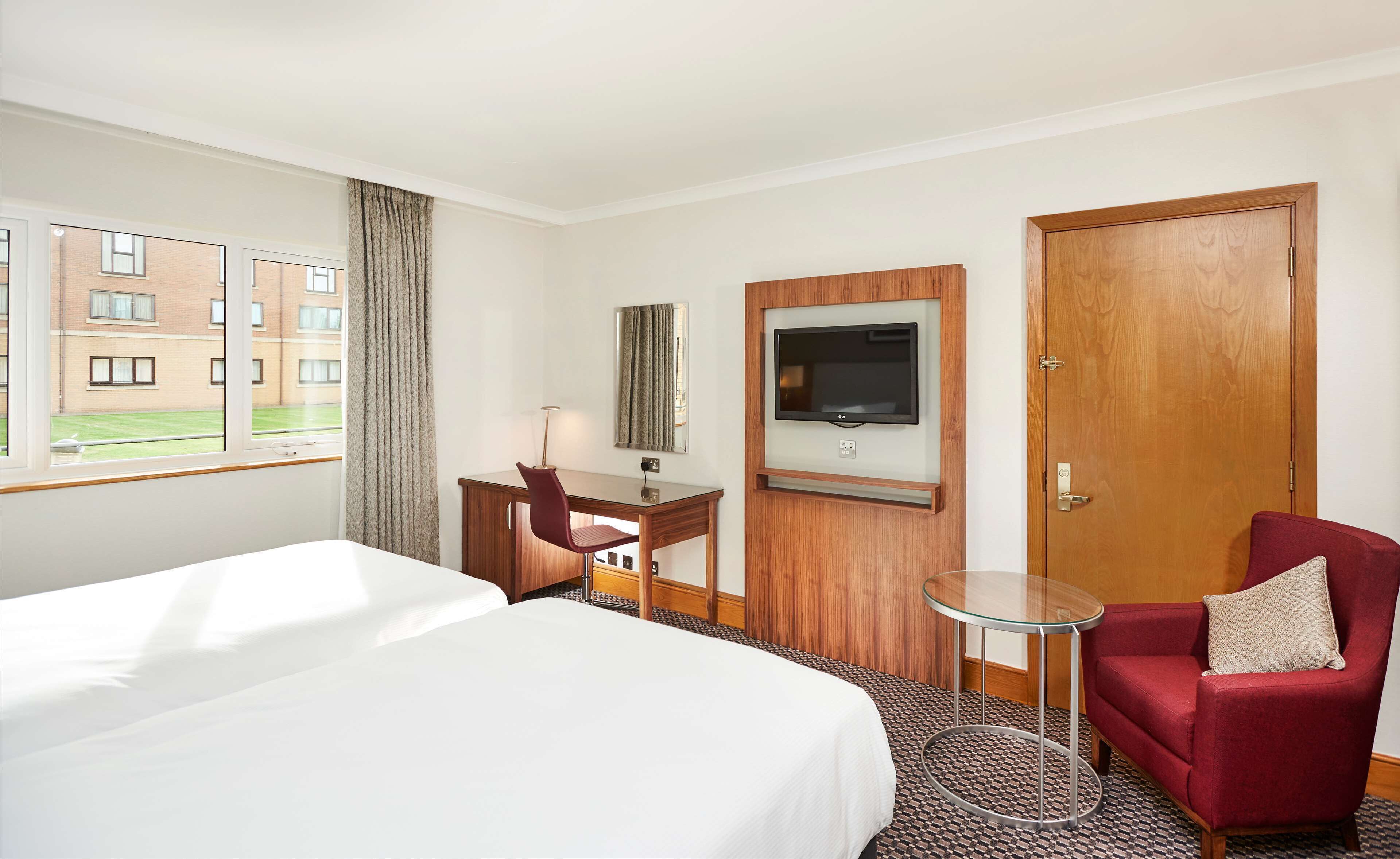 A hotel room with a large bed, a desk with a chair, a TV mounted on the wall, and a door.
