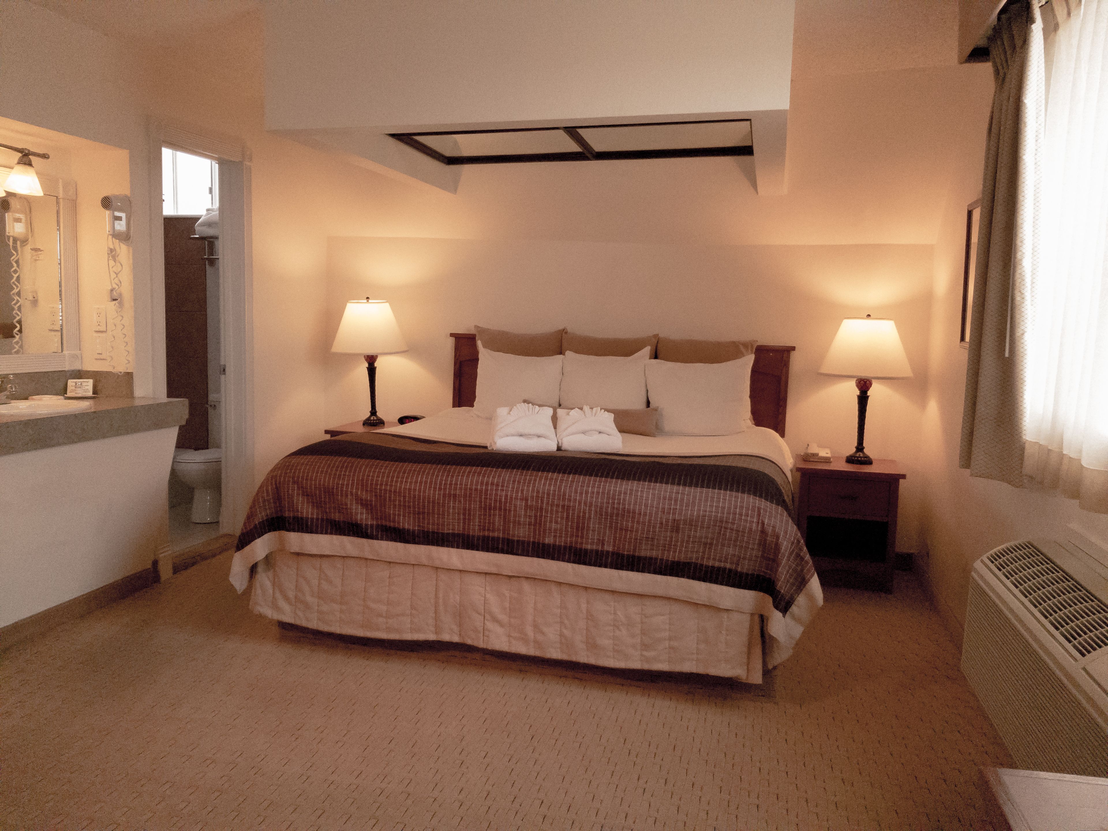 Une chambre d’hôtel avec un grand lit, deux lampes de chevet, un miroir et une fenêtre avec des rideaux.