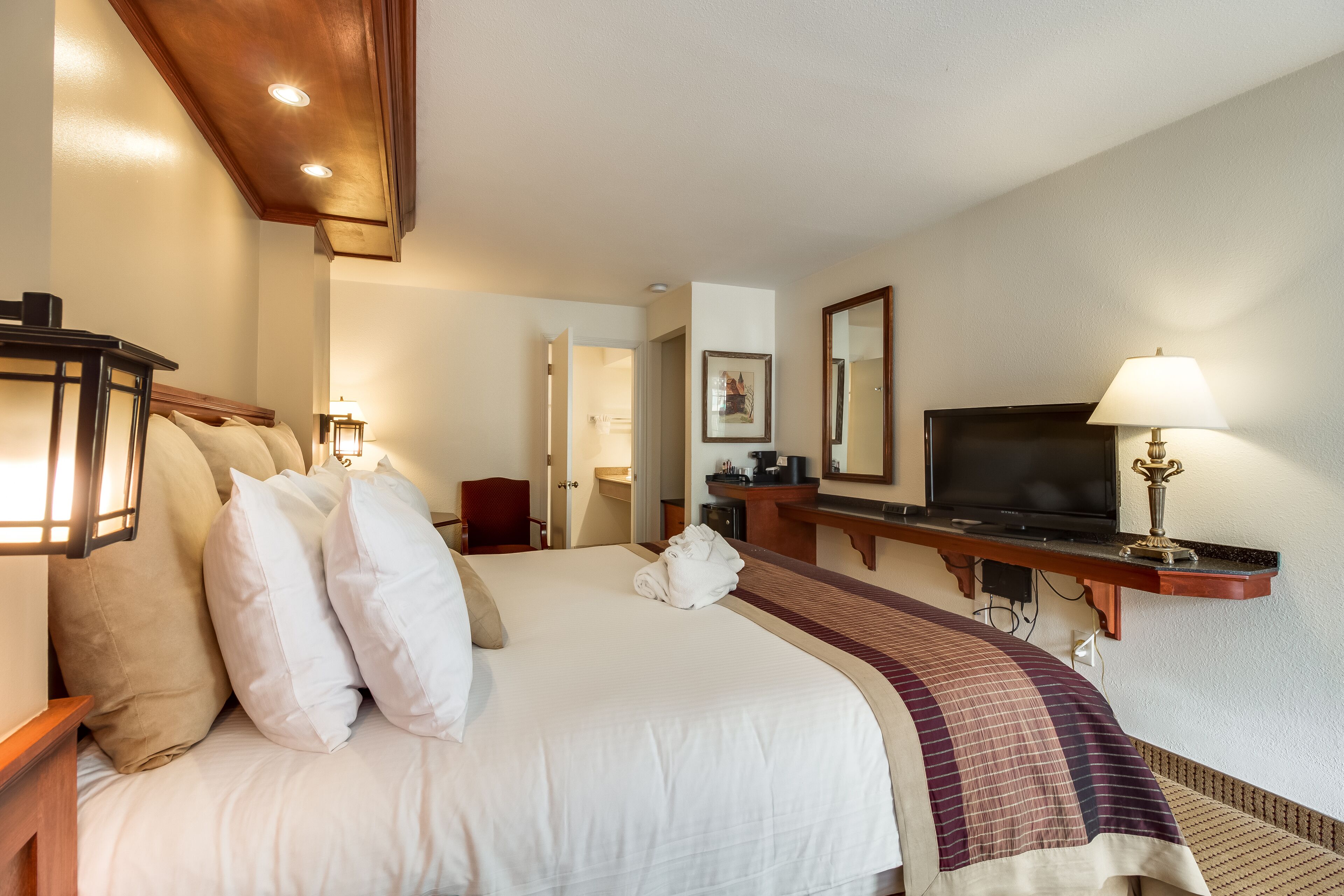 Habitación de hotel con una cama grande, televisión, escritorio con lámpara y espejo.