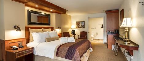 A hotel room with a large bed, bedside tables, a desk, and a mirror.