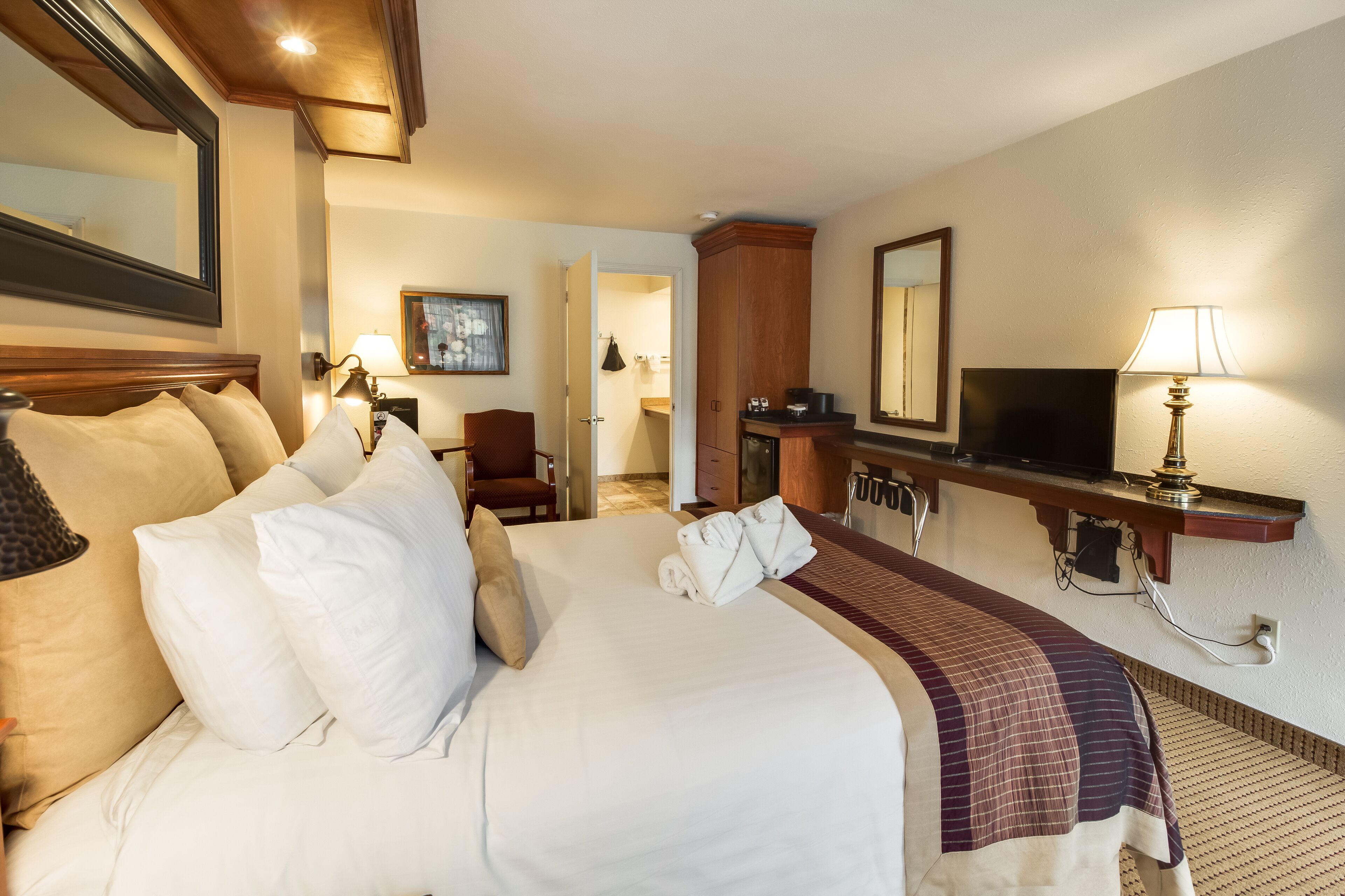 A hotel room with a large bed, a desk, a chair, a television, and a mirror.