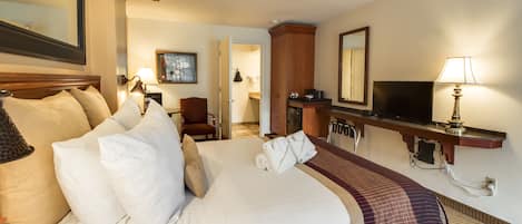 A hotel room with a large bed, a desk, a chair, a television, and a mirror.