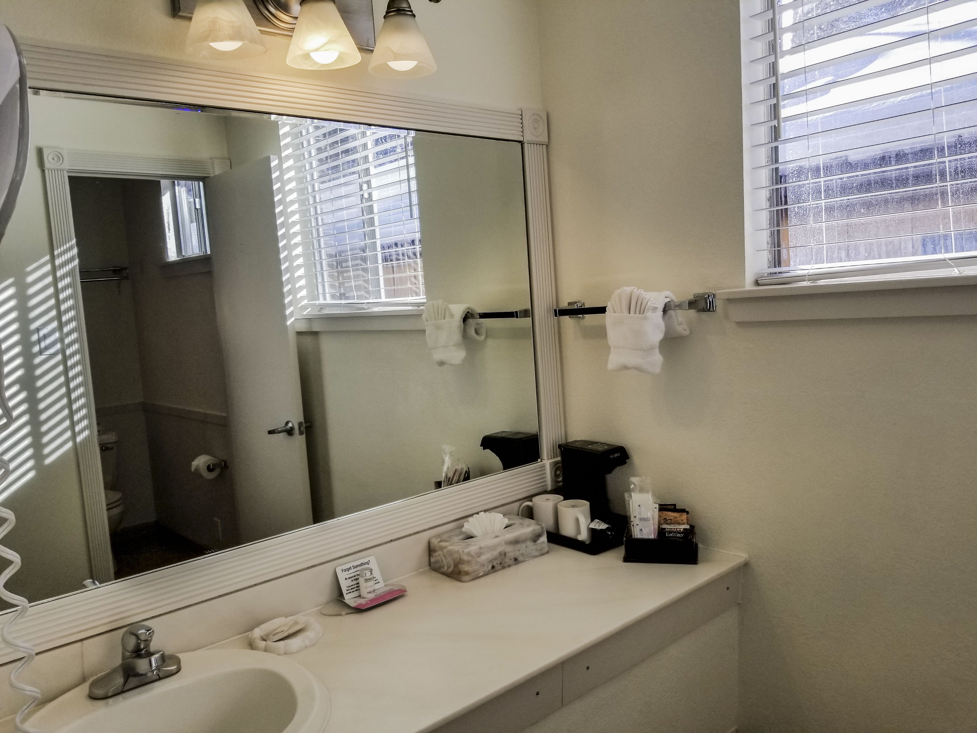 Een badkamer met een grote spiegel, een wastafel, een handdoekhouder en een raam met zonwering.