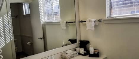 A bathroom with a large mirror, a sink, a towel rack, and a window with blinds.