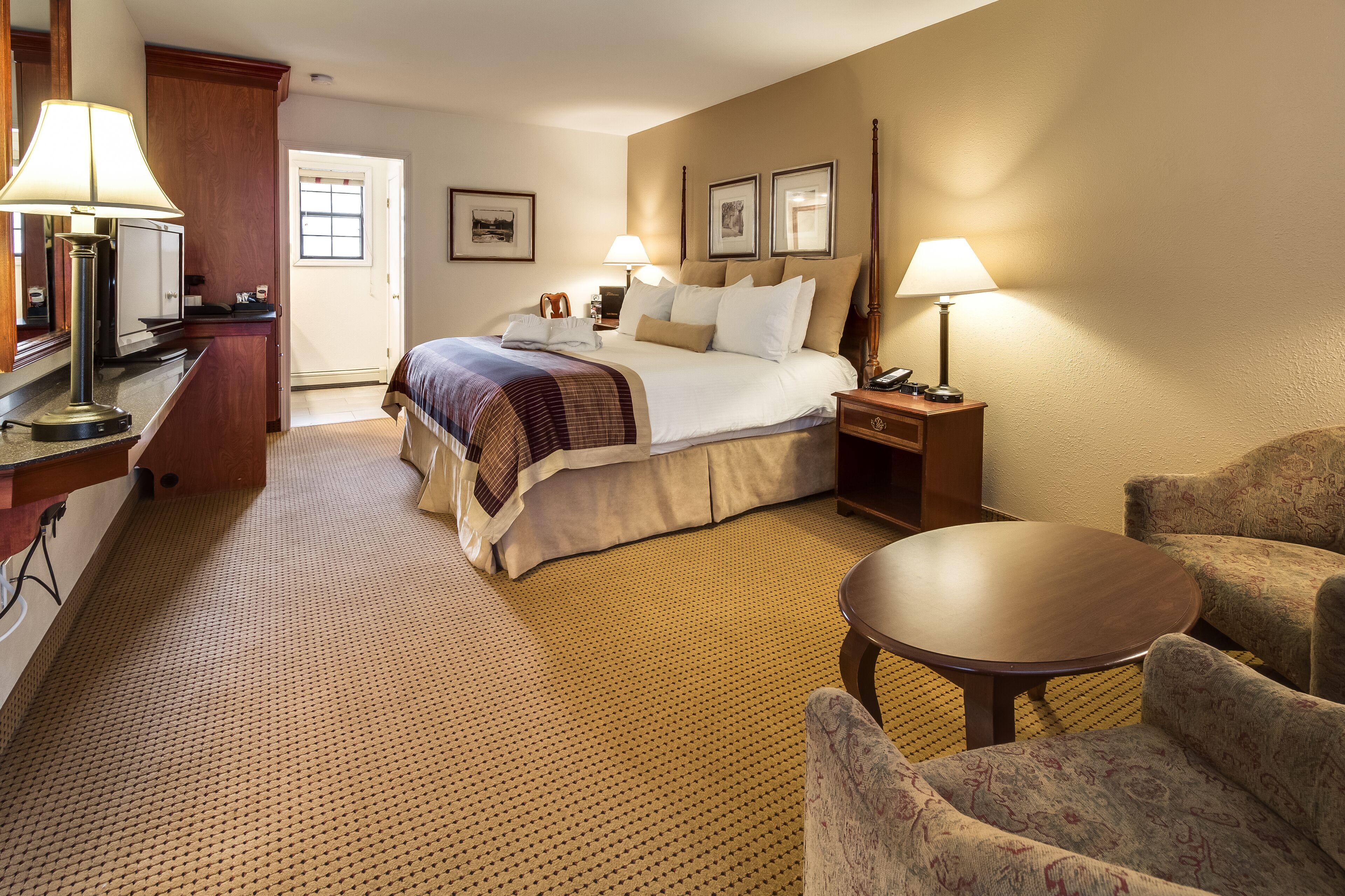 A hotel room with a bed, two bedside tables, a desk, a chair, and a small table.