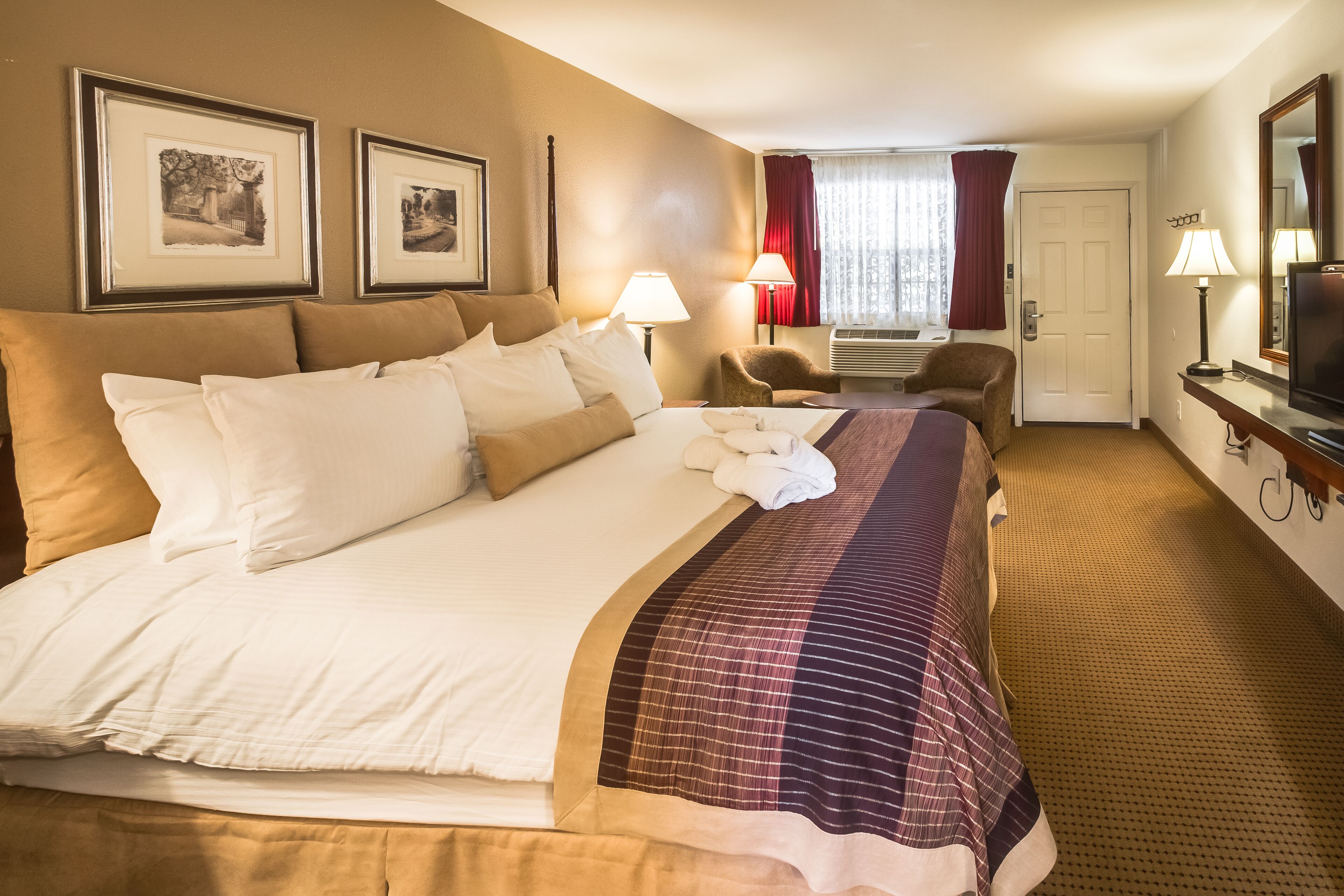 A hotel room with a large bed, two bedside lamps, a chair, a television, and framed pictures on the wall.