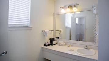 Un baño con lavamanos blanco, un espejo grande y una ventana con persianas.