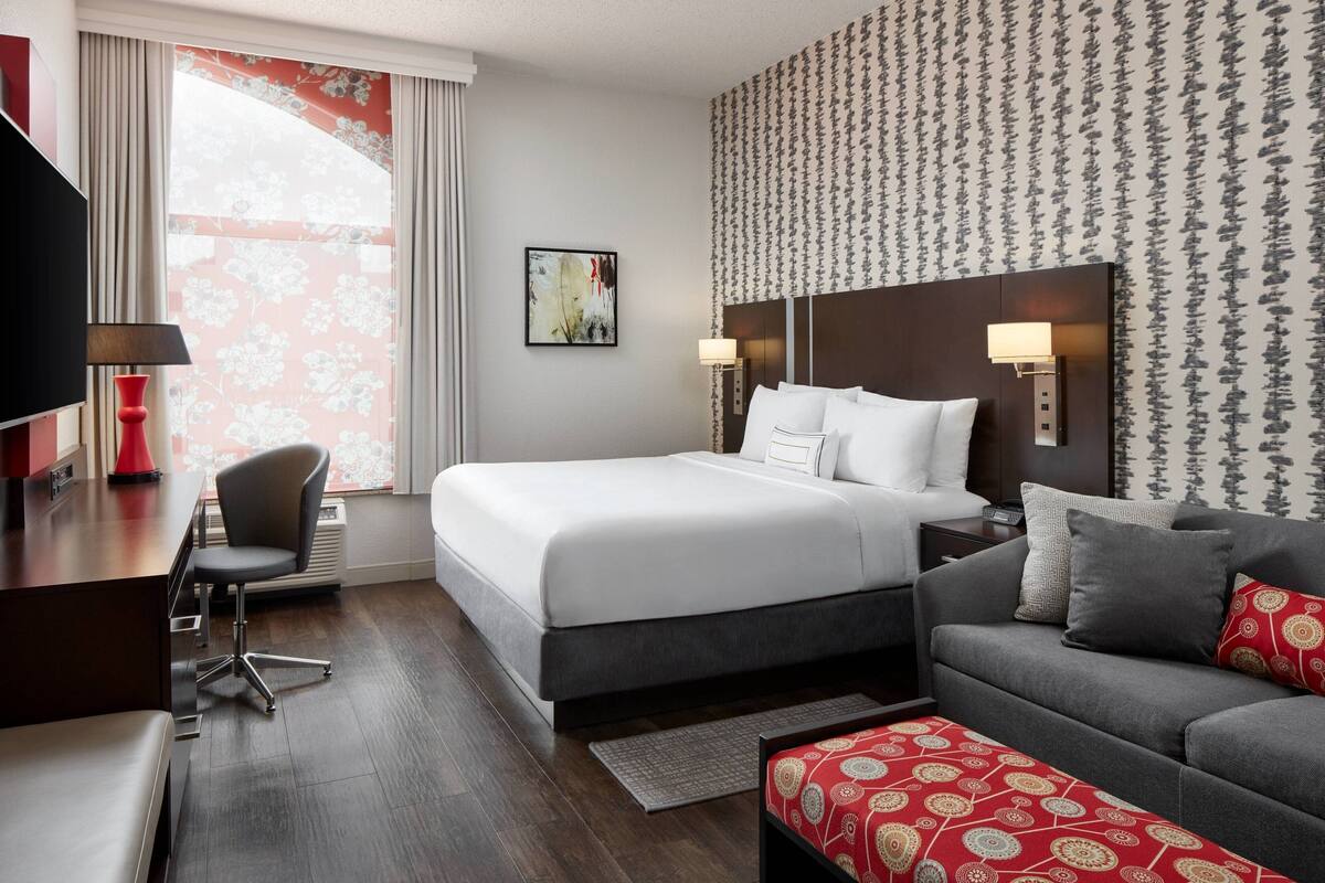 Quarto de hotel com cama, sofá, escrivaninha e televisão.