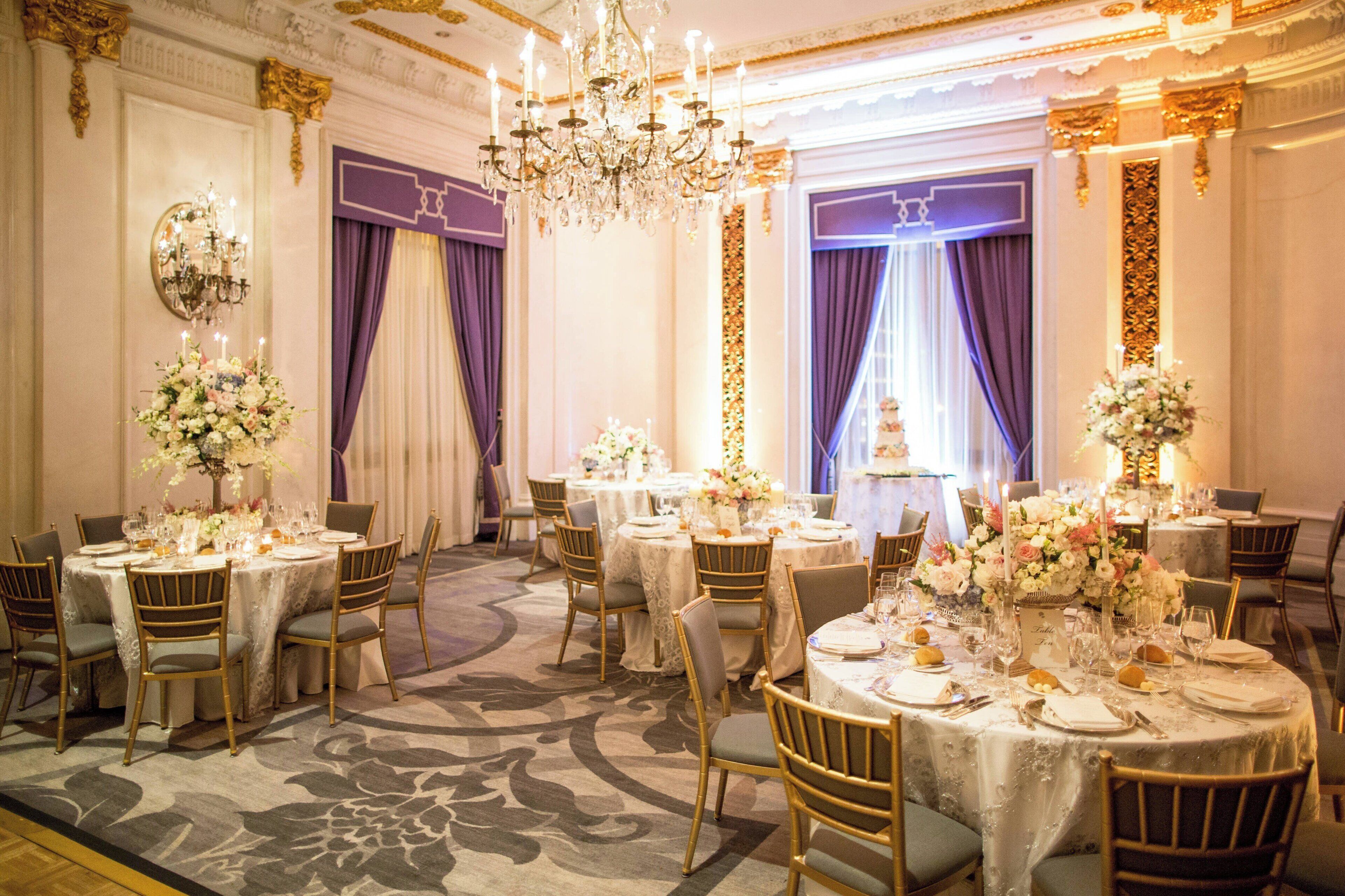 A formal dining room with round tables, gold chairs, and floral centerpieces.
