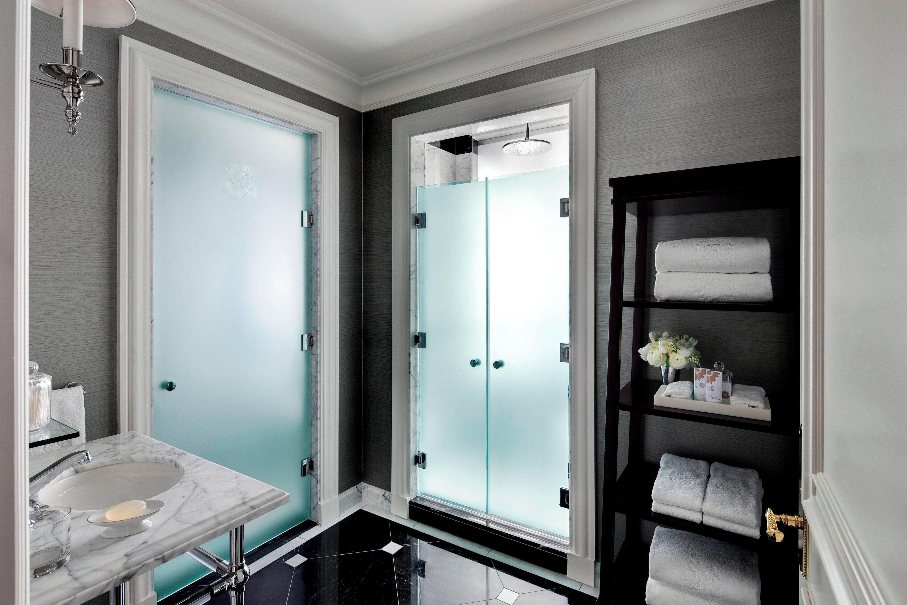 A modern bathroom with a marble sink, frosted glass doors, a glass shower enclosure, and a towel rack with neatly folded towels.